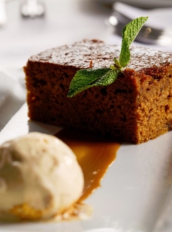 close up of sticky toffee pudding and ice cream on a white plate