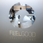 Feel Good Health Club branding on frosted glass door, showing gym equipment behind