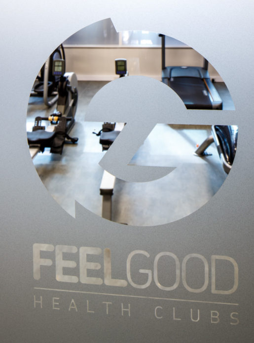 Feel Good Health Club branding on frosted glass door, showing gym equipment behind